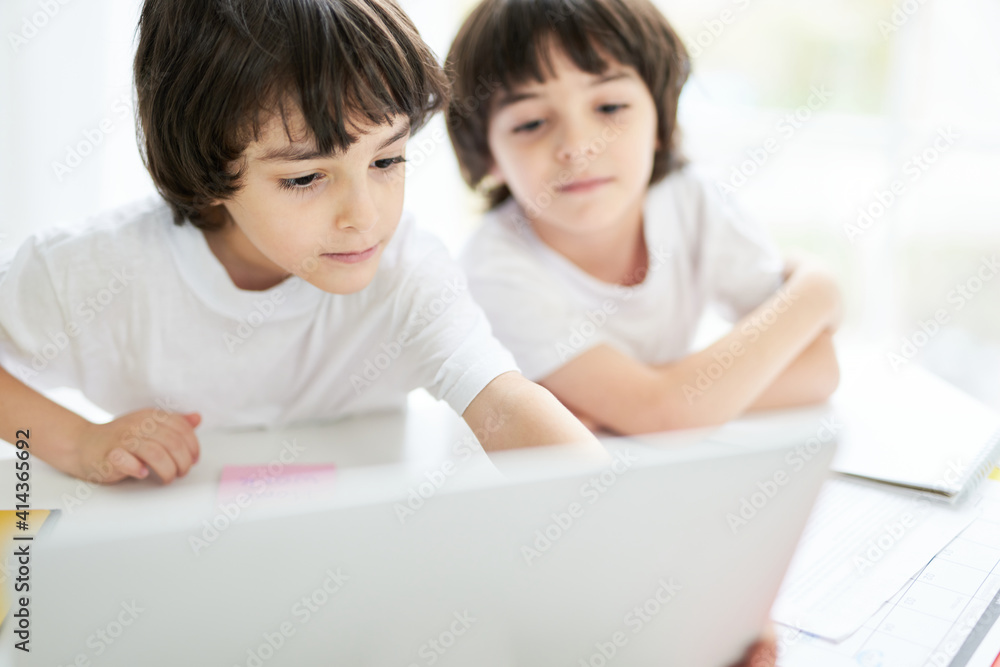 Education for kids. Cute latin boy looking focused, sitting with his brother at the table, looking at the screen of laptop. Two little children having online lesson at home Education for kids. Cute latin boy looking focused, sitting with his brother at the table, looking at the screen of laptop. Two little children having online lesson at home