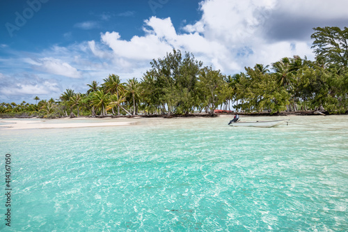 Atoll of Fakarava Island with small anchored boat at beautiful palm tree beach in French Polynesia.
