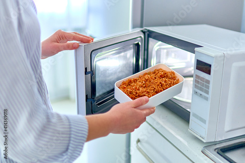 Female hands warming up a container of food in the modern microwave oven for snack lunch at home