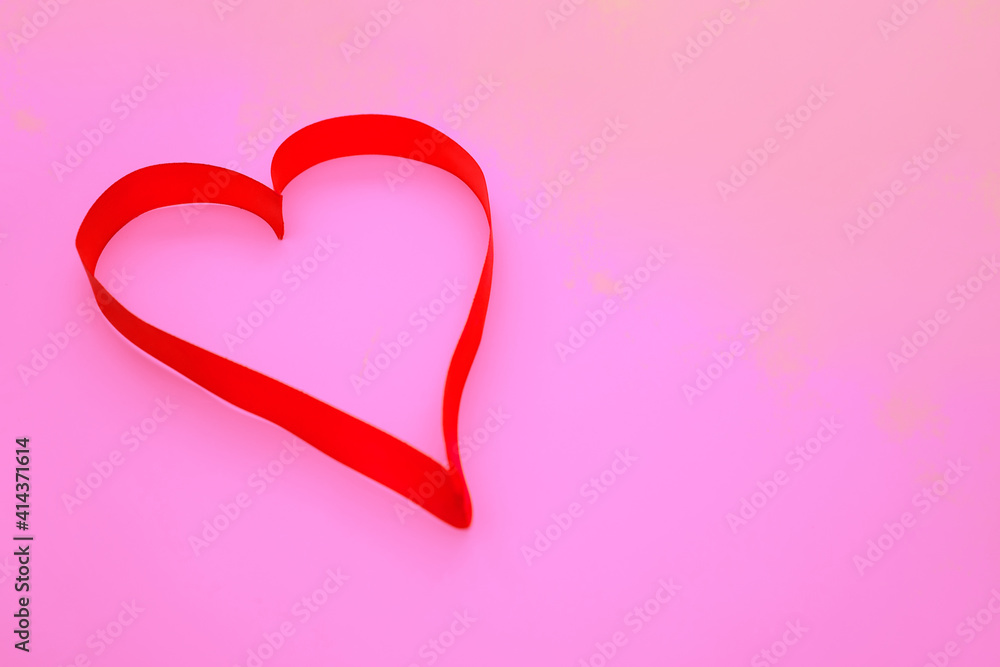 On a pink background, a pink satin ribbon in the shape of a heart.Gift wrap.