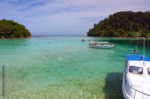 Transparent turquoise sea water in the foreground, boat on the water, tropical vegetation jungle in the background © KANSTANTSIN