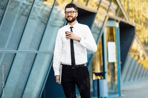 business man with laptop holding coffee in hand near office