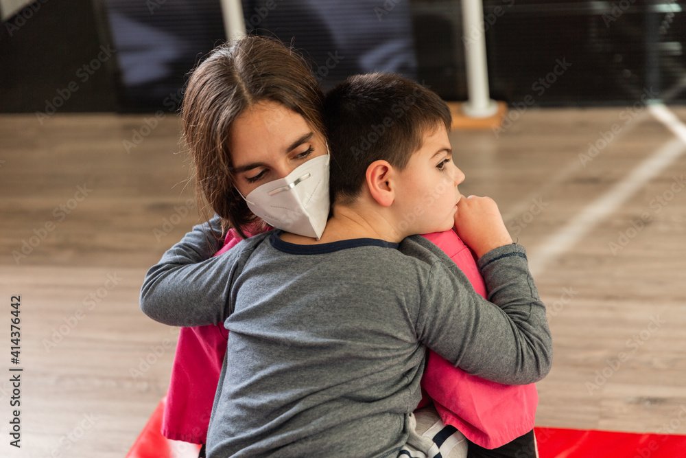 child with disabilities is hugged by physiotherapist wearing protective mask