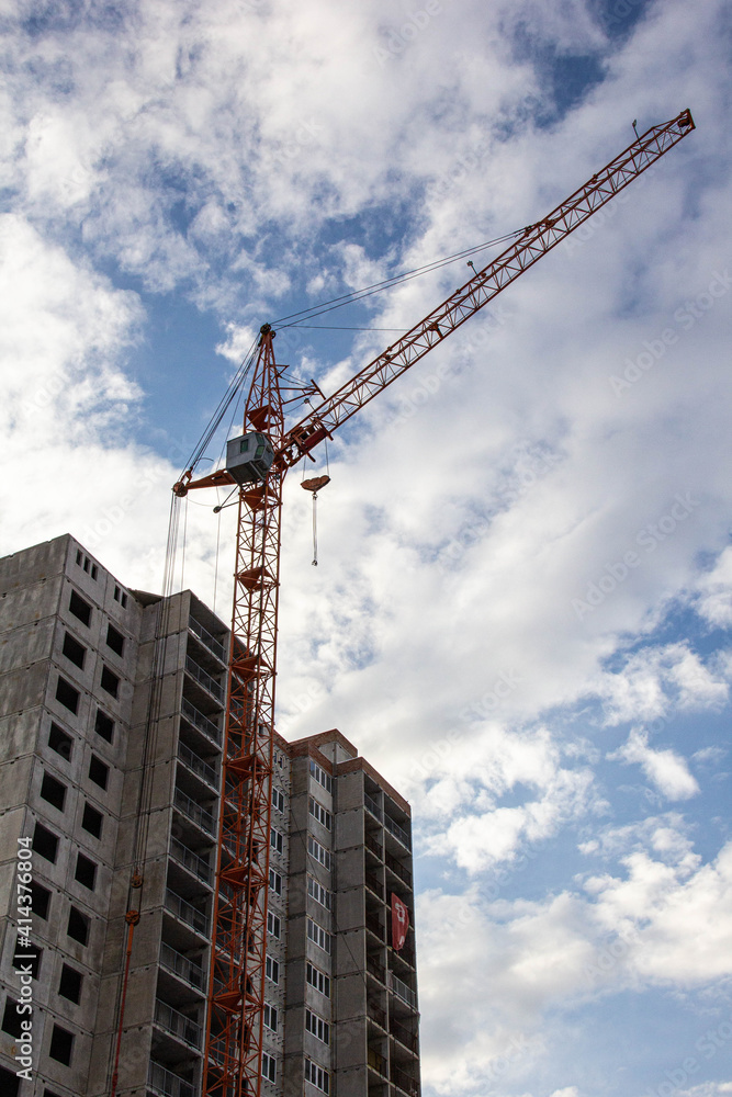 A crane near a house under construction against the blue sky. A crane near a house under construction against the blue sky.