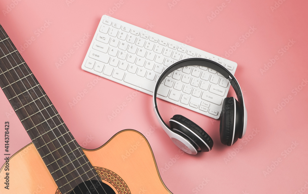 computer keyboard, headphones and acoustic guitar on pink background with copy space. Musician, leisure and online music learning concept. computer keyboard, headphones and acoustic guitar on pink background with copy space. Musician, leisure and online music learning concept.