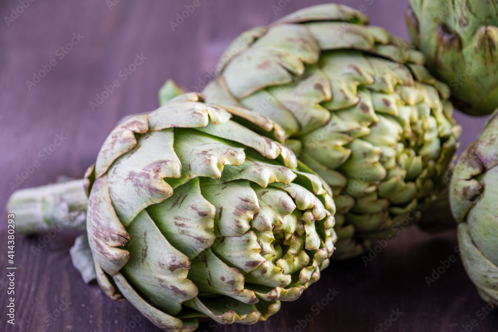 Fototapeta premium Close-up of several green artichokes, with selective focus, on wooden table, horizontal