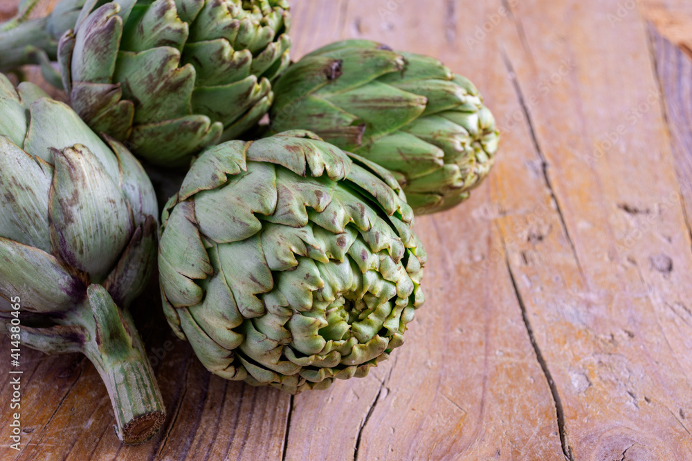 Fototapeta premium Top view of green artichokes, with selective focus, on rustic wooden table, horizontal, with copy space