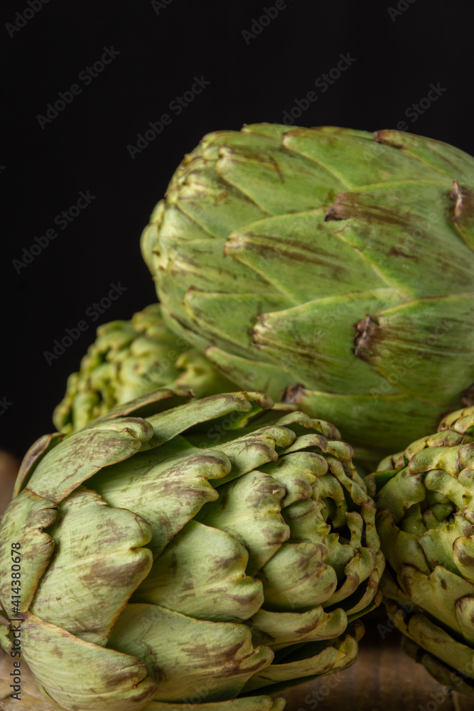 Fototapeta premium Close-up of a group of green artichokes, with selective focus, black background, vertical, with copy space