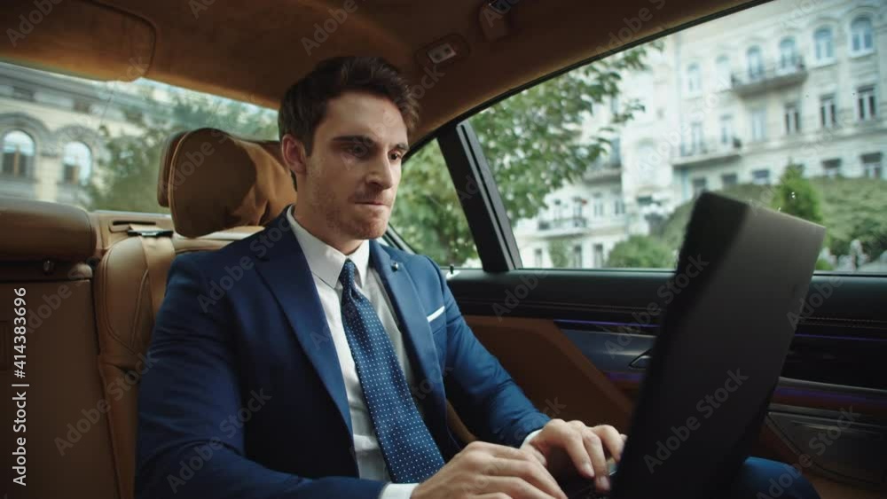Angry male ceo typing laptop computer in luxury car. Businessman feeling angry Angry male ceo typing laptop computer in luxury car. Businessman feeling angry