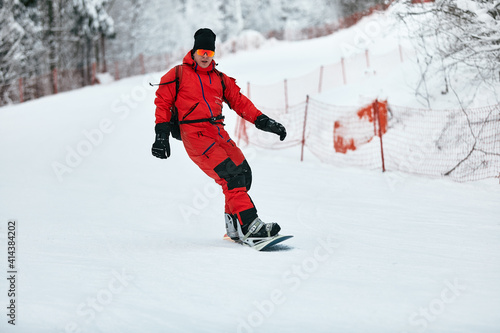 Male snowboarder in a red suit rides on the snowy hill with snowboard, Skiing and snowboarding concept