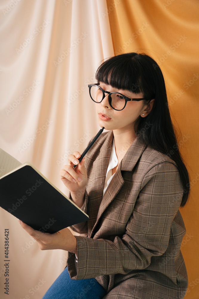 Obraz premium Thoughtful Beautiful asian thai long dark hair woman in jacket suit hold a book and pen.
