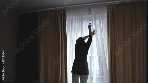 The housekeeper opens the curtains at the hotel room.