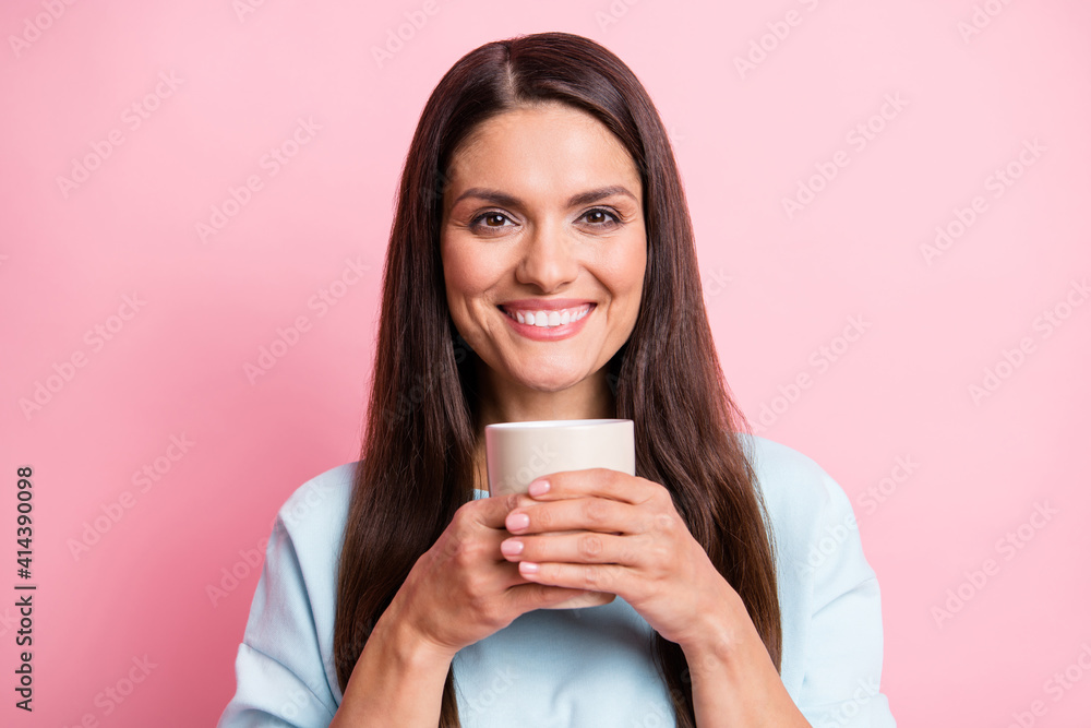 Photo portrait of smiling pretty woman keeping mug with beverage wearing blue jumper isolated on pastel pink color background Photo portrait of smiling pretty woman keeping mug with beverage wearing blue jumper isolated on pastel pink color background