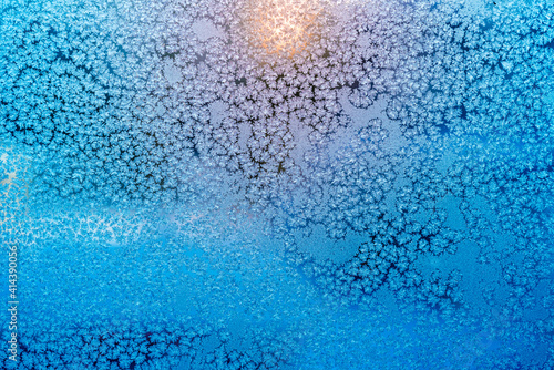 Ice patterns on a frozen window and light from the rising sun outside the window - winter background