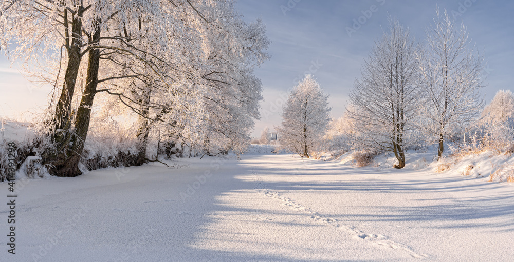 Rural Winter Landscape In Pastel Colors With Frozen River, Surrounded By Snowy Trees And Small Wood House On The River Bank. Christmas Landscape With Frozen Pond And Traces Of Animals Over Snow. Rural Winter Landscape In Pastel Colors With Frozen River, Surrounded By Snowy Trees And Small Wood House On The River Bank. Christmas Landscape With Frozen Pond And Traces Of Animals Over Snow.