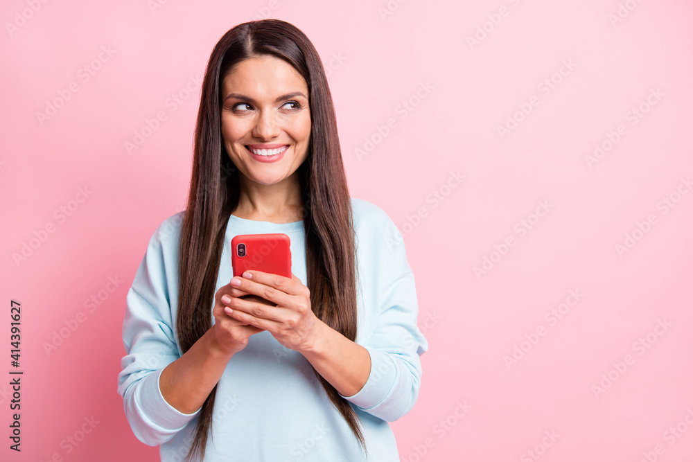 Photo portrait of brunette using cellphone texting sms looking empty space isolated on pastel pink color background Photo portrait of brunette using cellphone texting sms looking empty space isolated on pastel pink color background