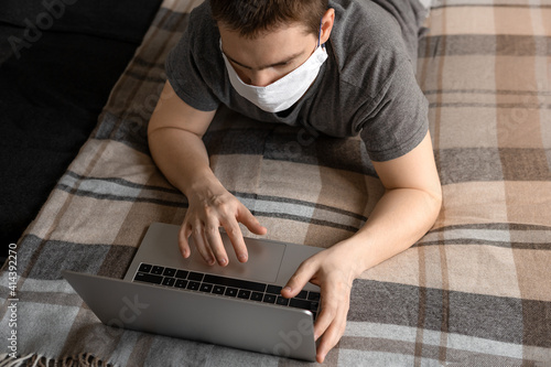 The man in the mask works with the laptop lying on the bed