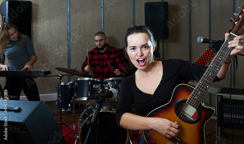 Group of young musicians with passionate emotional woman vocalist and guitarist practicing in rehearsal room