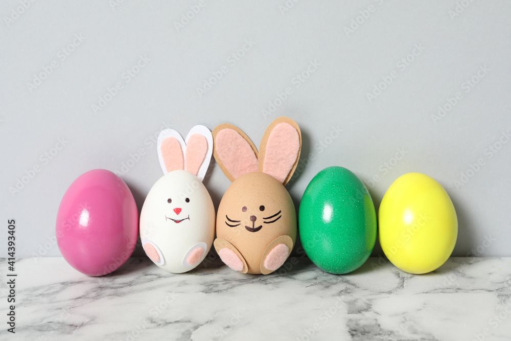 Two eggs as cute bunnies among others on white marble table against light grey background. Easter celebration Two eggs as cute bunnies among others on white marble table against light grey background. Easter celebration