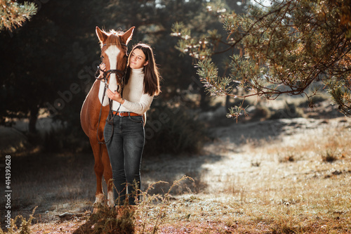Beautiful young girl posing with her horse in the nature. Sunny autumn day.