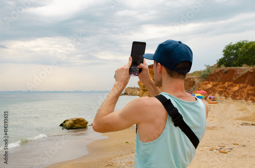 Man catching signal on the wild beach, making photo of seascape. back wiew photo