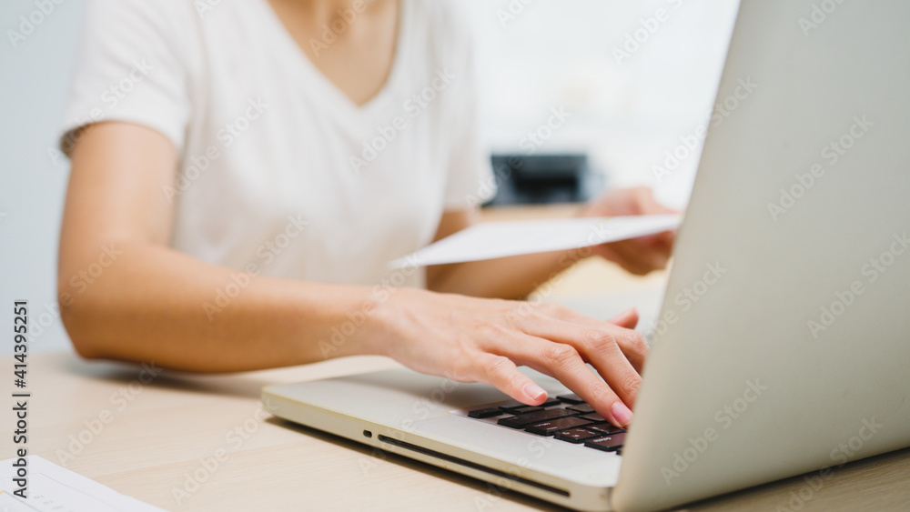 Fototapeta premium Freelance young Asia businesswoman casual wear using laptop working in living room at home. Working from home, remotely work, self isolation, social distancing, quarantine for corona virus prevention.