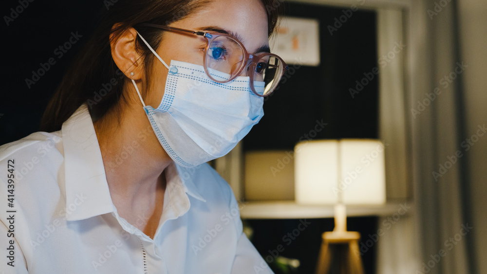 Freelance Asia lady wear medical face mask use laptop hard work in living room at house. Working from home overload at night, remotely work, social distancing, quarantine for corona virus prevention. Freelance Asia lady wear medical face mask use laptop hard work in living room at house. Working from home overload at night, remotely work, social distancing, quarantine for corona virus prevention.