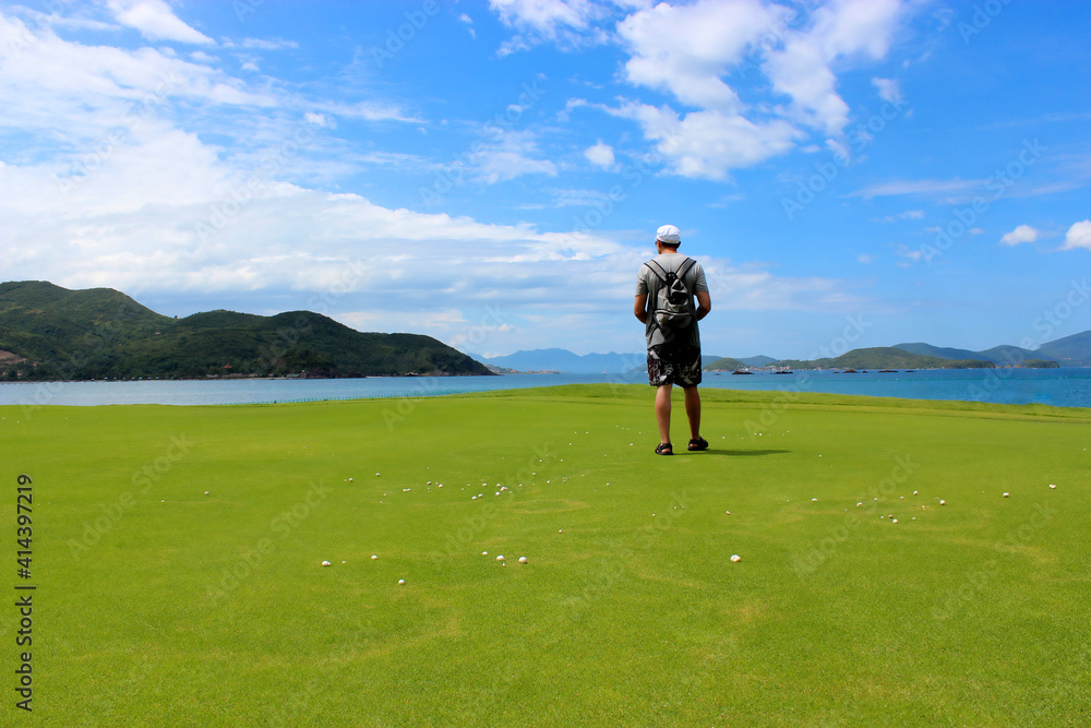the guy stands with his back on the golf course and looks at the sea