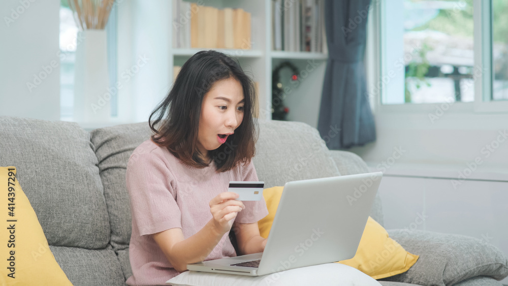 Asian woman using laptop and credit card shopping ecommerce, female relax feeling happy online shopping sitting on sofa in living room at home. Lifestyle women relax at home concept. Asian woman using laptop and credit card shopping ecommerce, female relax feeling happy online shopping sitting on sofa in living room at home. Lifestyle women relax at home concept.