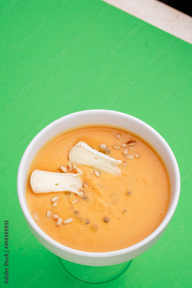 Pumpkin soup with eringi mushrooms in white plate on green background. Close-up. Top view. Space for text. Photo for cutting, for menu Pumpkin soup with eringi mushrooms in white plate on green background. Close-up. Top view. Space for text. Photo for cutting, for menu
