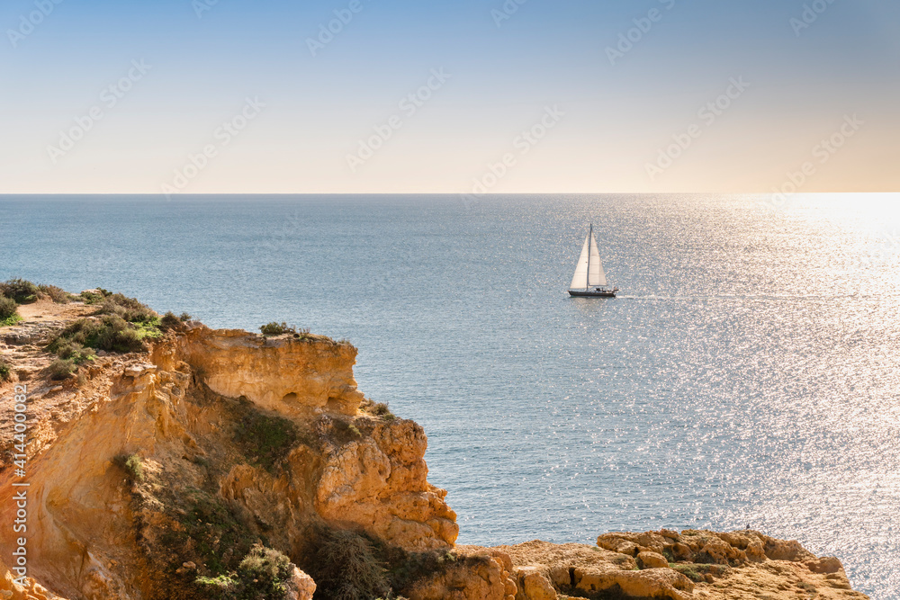 Boat sailing on Atlantic Ocean by the cliffs of Algarve, Portugal