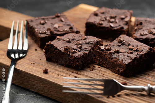 Vegan chocolate brownies with dry srawberries pieces and choco drops with old silverware on dark background photo