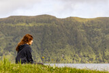 Girl sitting in grass, by Sete Cidades lake, enjoying the landscape, peacefully.