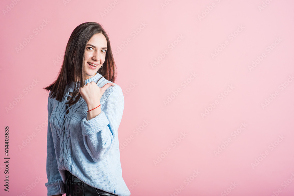 Portrait of a brunette girl on a pink background who points her thumb to copyspace Portrait of a brunette girl on a pink background who points her thumb to copyspace