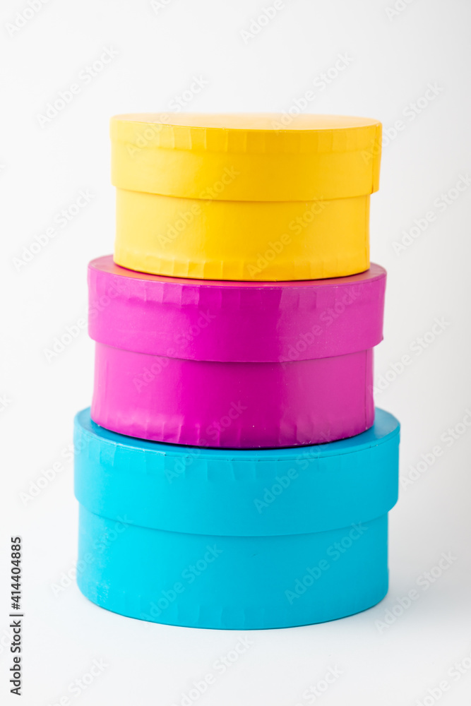 Close-up of round blue, yellow and purple boxes, stacked, on white background, vertically, with copy space Close-up of round blue, yellow and purple boxes, stacked, on white background, vertically, with copy space