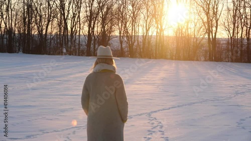 stylish girl in white coat and hat on a snowy field at sunset time