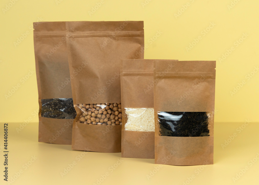 Brown kraft paper doypack bags with groceries front view on a yellow  background. Packaging for foods and goods template mock-up. Packs with  windows for weight products. Stock Photo | Adobe Stock