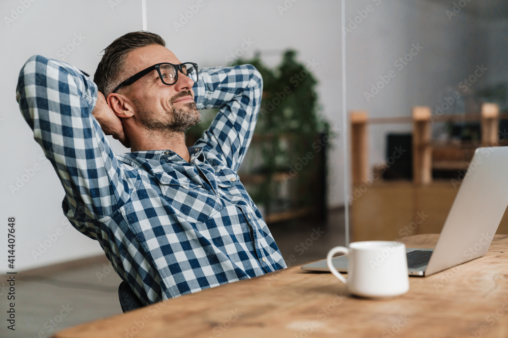 Pleased unshaven man in eyeglasses resting while working with laptop Pleased unshaven man in eyeglasses resting while working with laptop