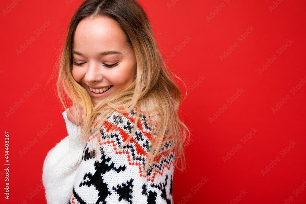Photo shot of young beautiful cute happy blonde woman wearing winter sweater isolated over red background with copy space. Christmas concept Photo shot of young beautiful cute happy blonde woman wearing winter sweater isolated over red background with copy space. Christmas concept