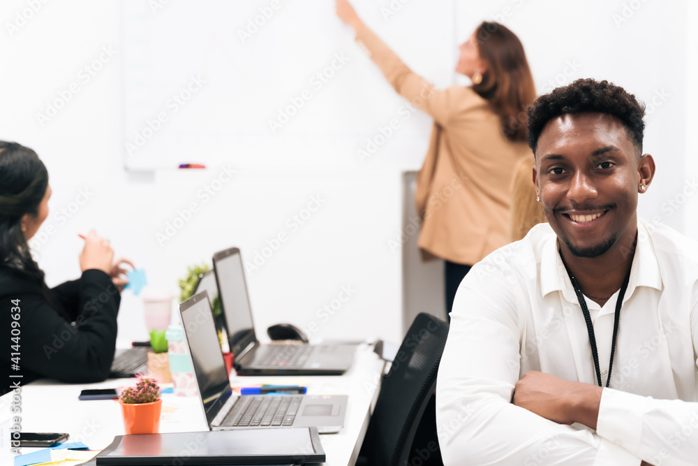 Young African male employee in formal clothes sitting in the office. Background teacher teaching. Job and university concept. Young African male employee in formal clothes sitting in the office. Background teacher teaching. Job and university concept.