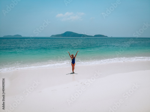 Young attractive woman in a blue swimming suit standing on a sandy beach and sunbathing. Summer vacation concept
