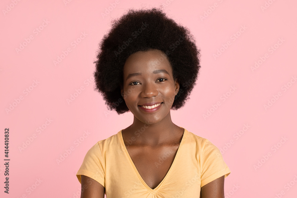 Portrait of young attractive african american woman, wearing yellow t-shirt, with afro hair and wide perfect smile on her face, posing to camera on pink pastel background. People, races concept Portrait of young attractive african american woman, wearing yellow t-shirt, with afro hair and wide perfect smile on her face, posing to camera on pink pastel background. People, races concept