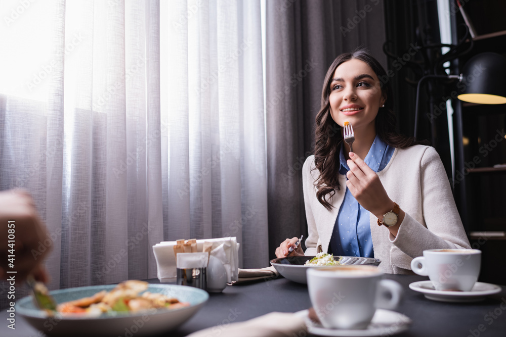 Smiling woman dinning with boyfriend on blurred foreground in restaurant