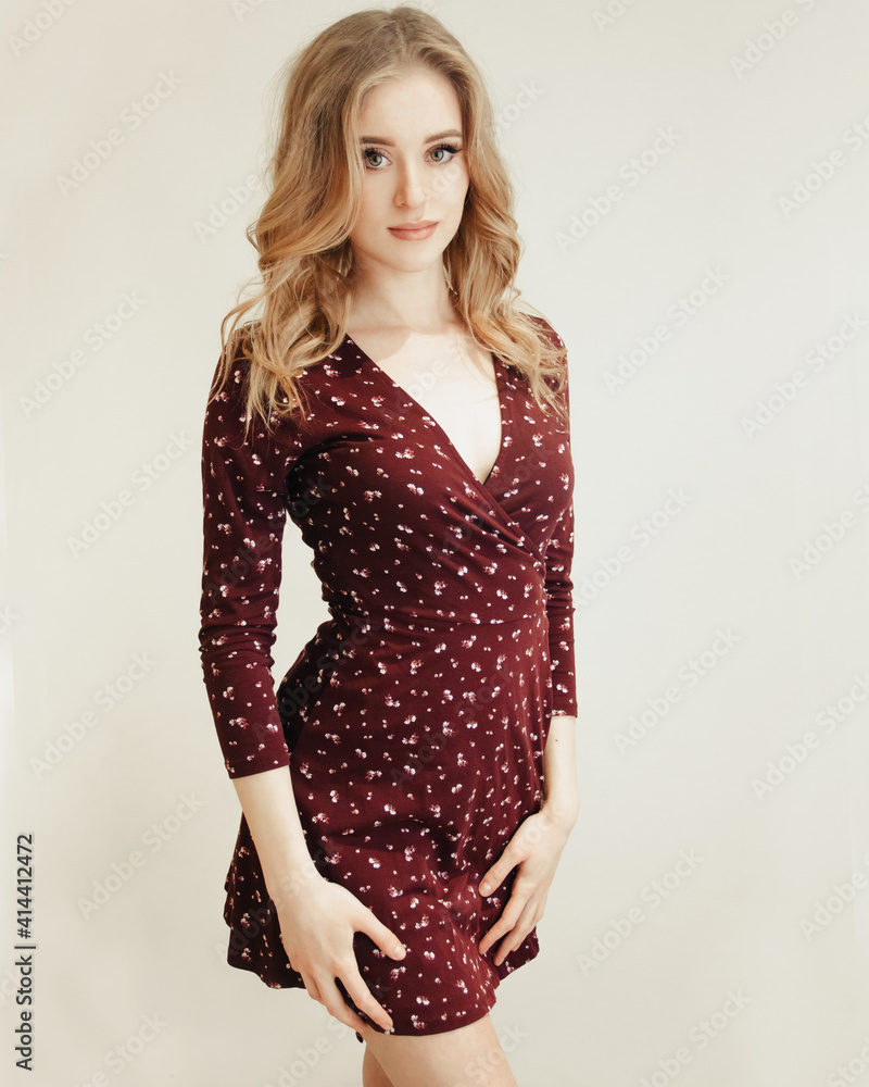  young blonde glamour girl in red spring dress is standing with flirt near white wall background, lifestyle concept, free space