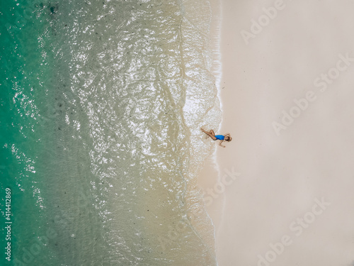 Young pretty woman in a blue swimming suit lying on a sandy beach during tide. Summer vacation concept