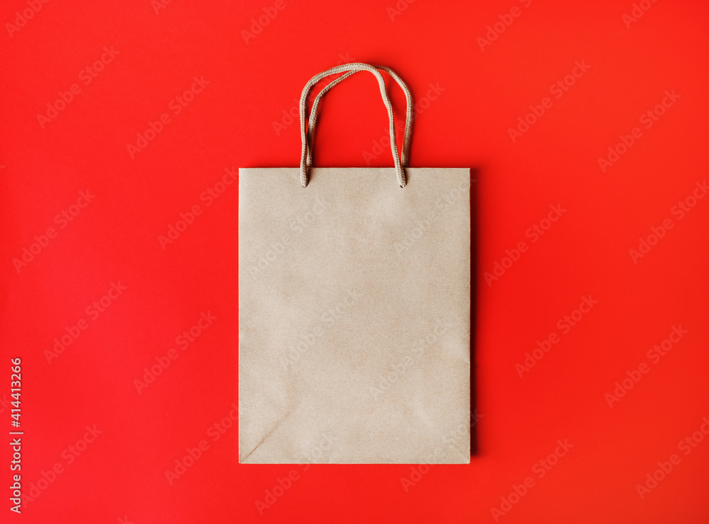 Blank brown paper bag with rope handles on red paper background. Top view. Flat lay. Blank brown paper bag with rope handles on red paper background. Top view. Flat lay.