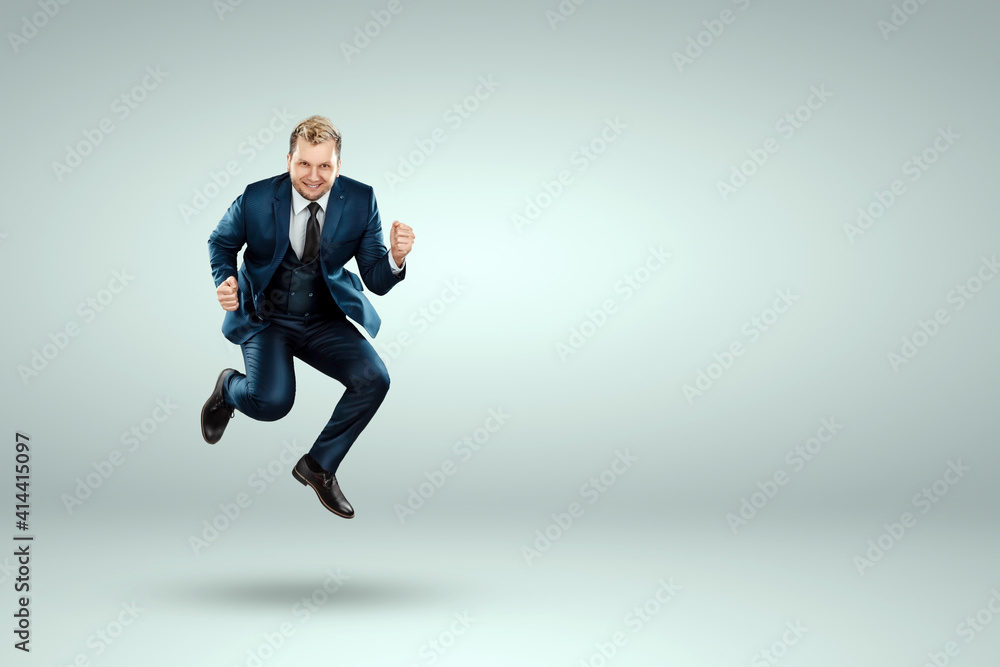 A man in a business suit jumps up cheerfully against a light background. The concept of joy, success, luck, winning.