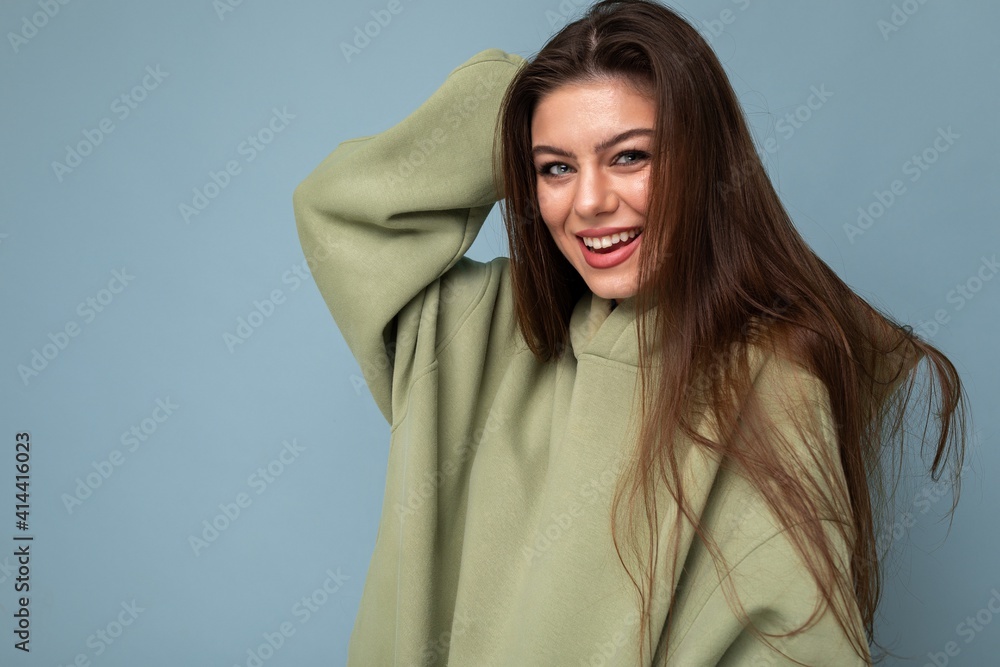 Portrait of young beautiful smiling girl in stylish hipster green hoodie. Sexy carefree woman posing near blue wall. Positive model having fun Portrait of young beautiful smiling girl in stylish hipster green hoodie. Sexy carefree woman posing near blue wall. Positive model having fun