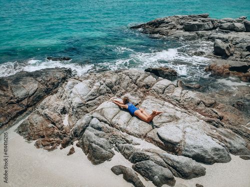 Pretty young woman in a blue swimming suit lying on the rocks in high tide. Summer vacation concept