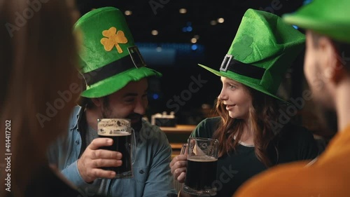 Portrait of friends in Irish hats celebrating Saint Patrick's Day in a pub. Men and women toasting with beer and having fun.